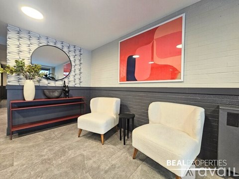 A living room with two chairs, a table, and a large abstract painting on the wall.