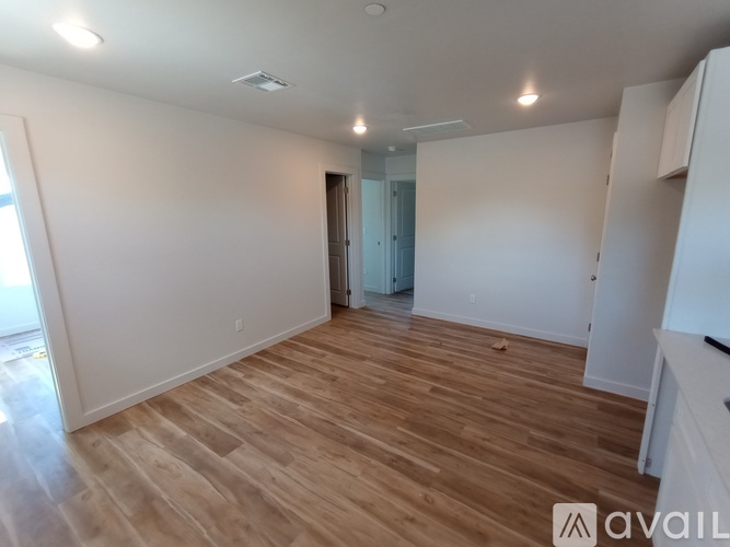 A room with wooden flooring and white walls, with a door in the background.