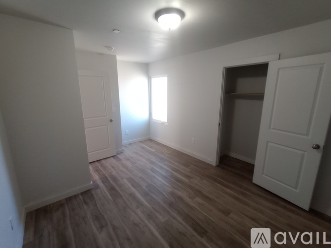 A room with wooden flooring and white walls, with a door on the right side.