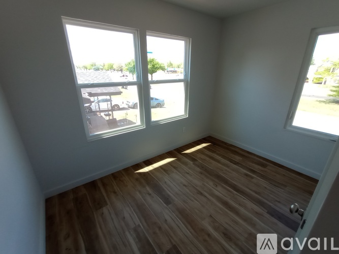 A room with wooden flooring and three windows overlooking a parking lot.