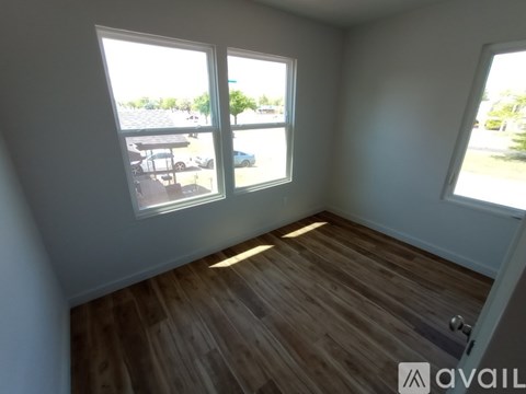 A room with wooden flooring and three windows overlooking a parking lot.