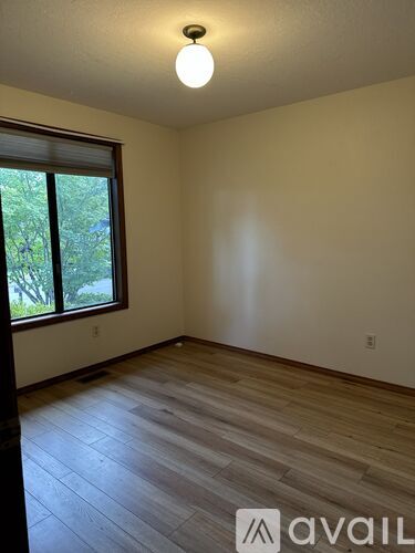 A room with wooden flooring and a window overlooking trees.