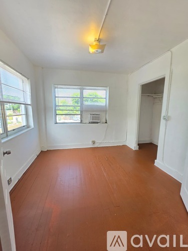 A room with wooden floors and white walls, with a window showing greenery outside.