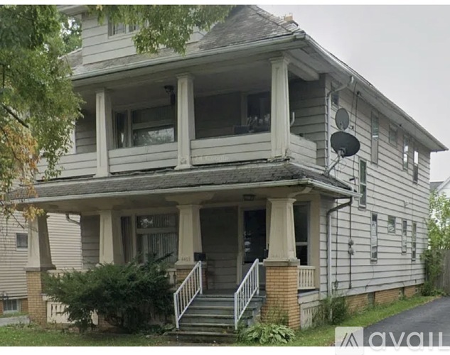 A two-story house with a porch and a satellite dish on the roof.