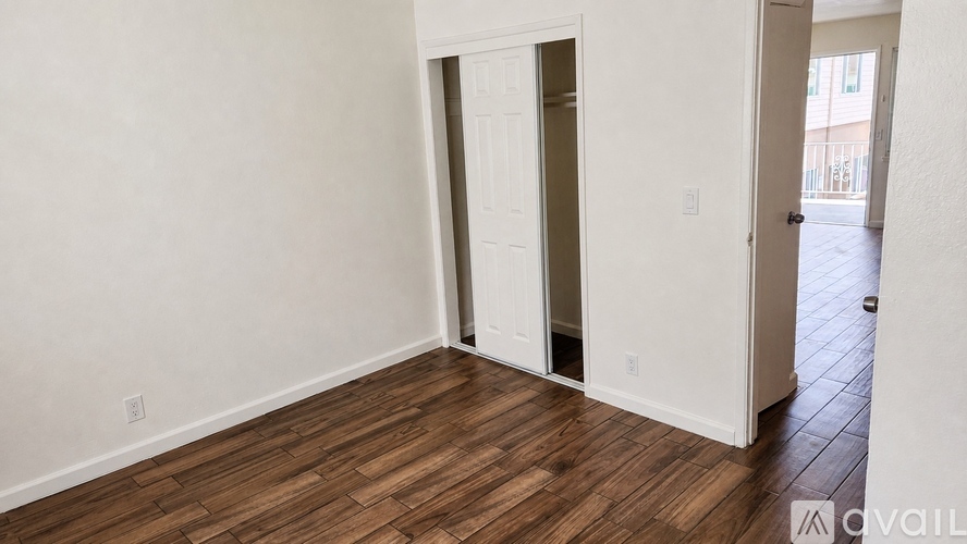 A room with a wooden floor and white walls with a door open to a hallway.