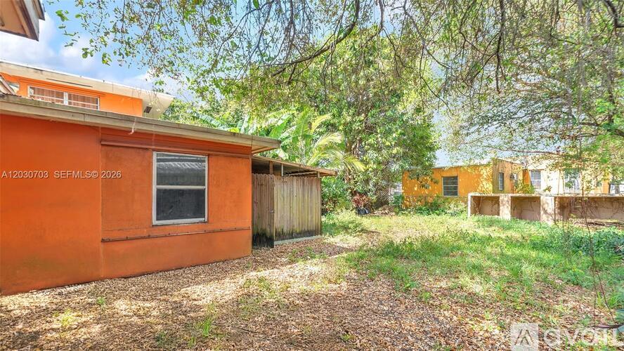 A small orange building with a window and a tree in front of it.