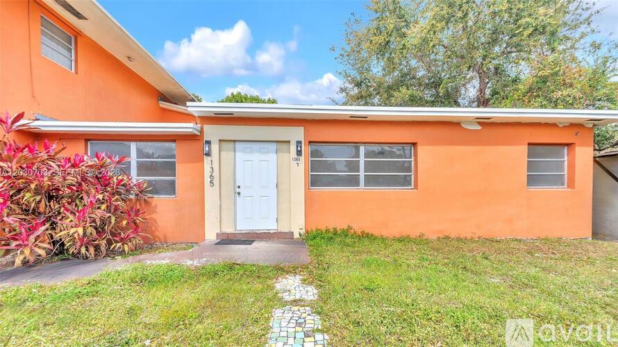A small orange house with a white door and windows, a green lawn, and a tree in the background.