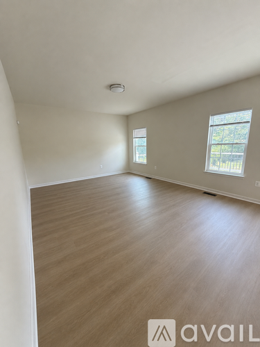 A room with wooden flooring and two windows.