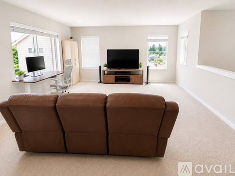 A brown couch sits in a living room with a television and a desk.