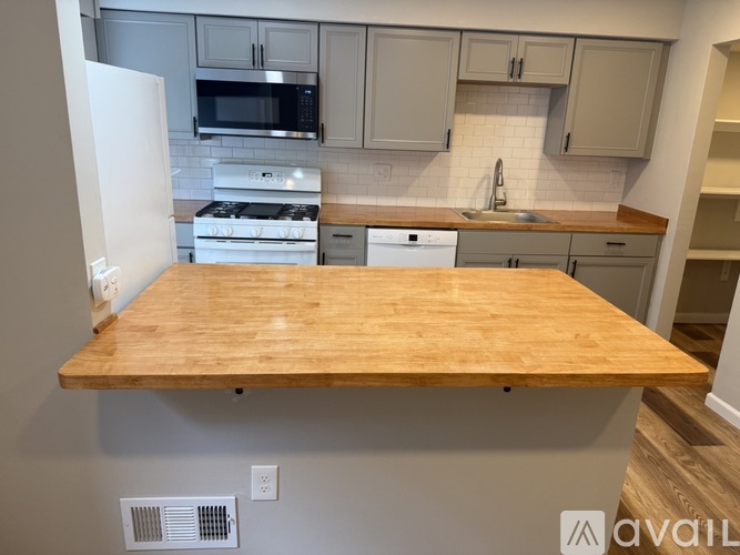 A kitchen with a wooden table in the foreground and a white fridge to the left.