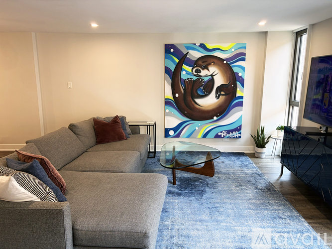 A living room with a grey couch and a painting of a otter.