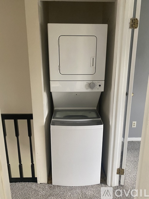 A white dishwasher is in a narrow space between a wall and a door.