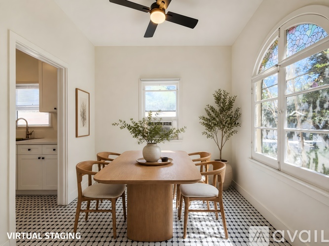 A dining room with a wooden table and chairs, a ceiling fan, and a window with a view of trees.