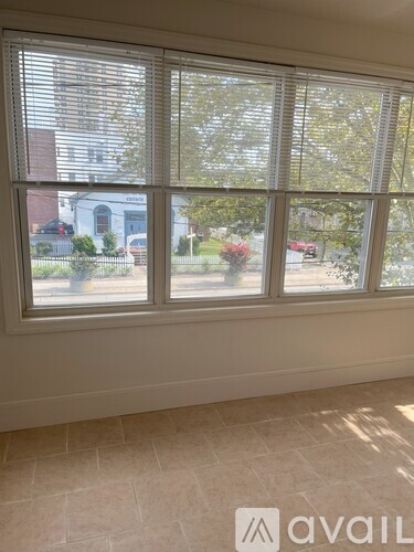 A window with blinds overlooking a street with cars and houses.