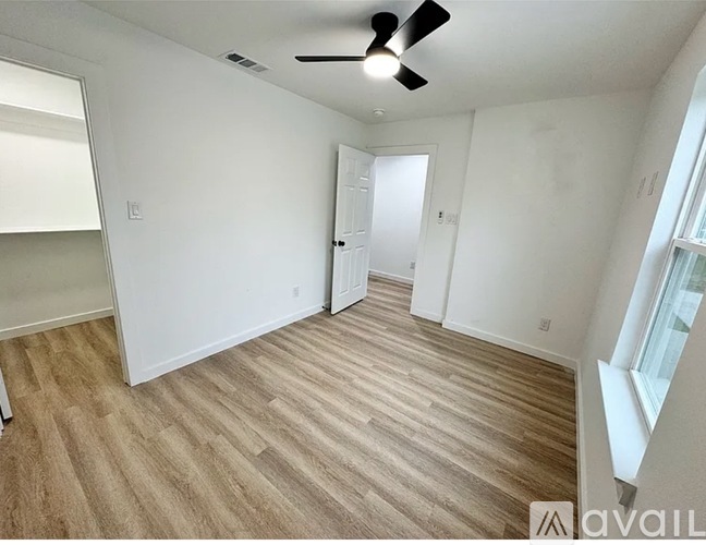 A room with a ceiling fan and light, wooden flooring, and a door leading to another room.