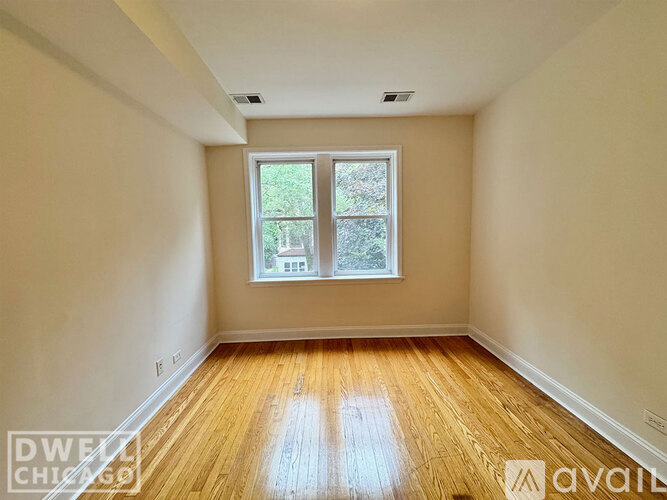A room with wooden floors and a window showing a view of trees and a building outside.
