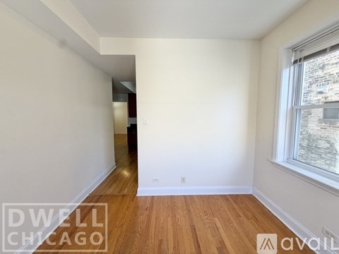 A room with white walls and wooden flooring, with a window on the right side.