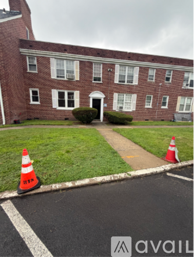 A building with a red brick facade and a white door is surrounded by a grassy area and a parking lot with orange traffic cones.