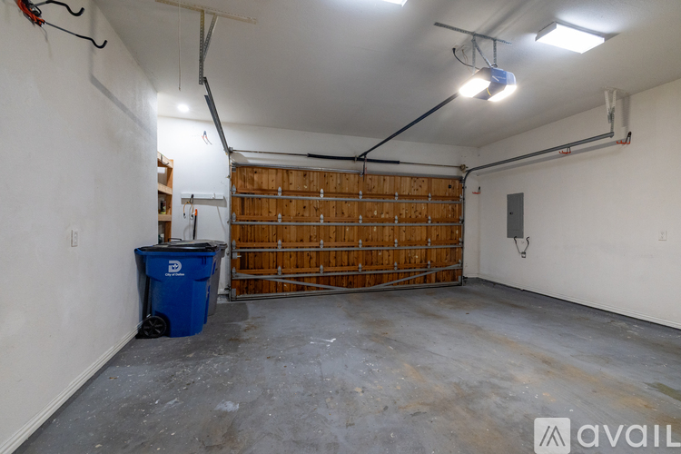 A large empty garage with a blue trash bin and wooden shelving in the background.