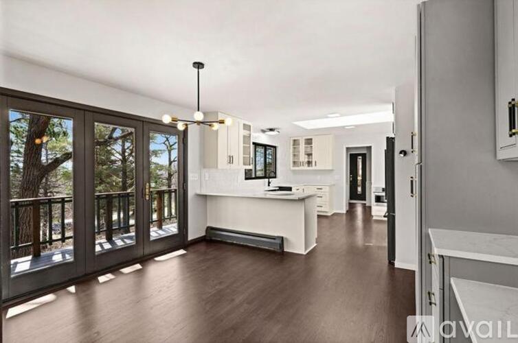 A spacious kitchen and living room with a view of trees through the sliding glass doors.