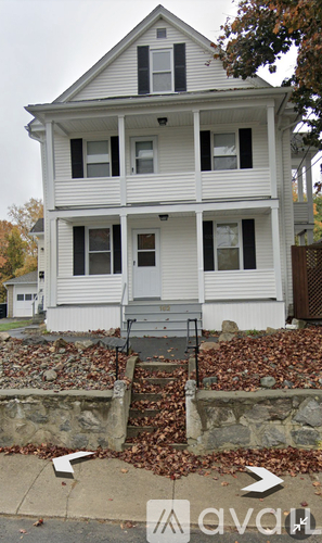 A two-story white house with a grey front door and a stone wall.