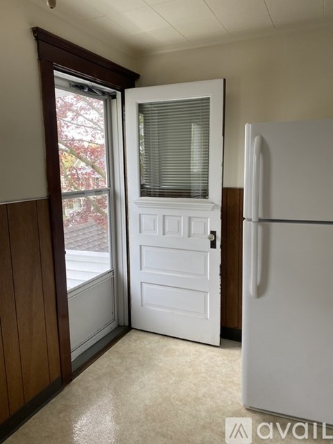 A white refrigerator is in a kitchen with a white door and a window.