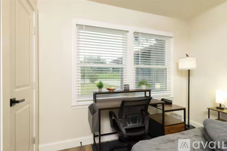 A room with a desk and chair in front of a window with blinds.