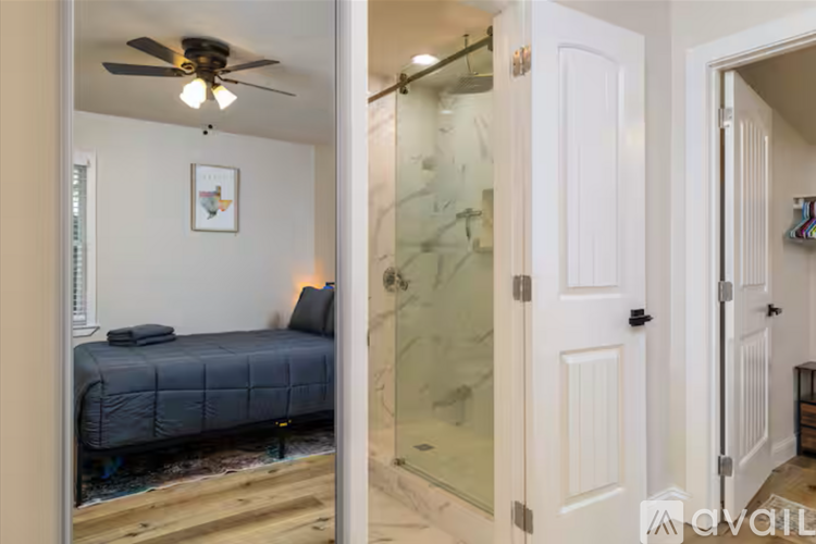 A bedroom with a bed, a ceiling fan, and a glass shower stall.