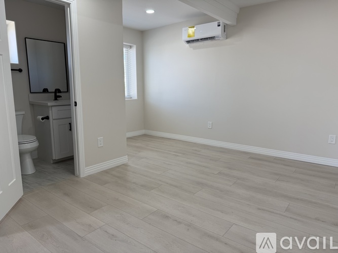 A spacious room with light wood flooring and a wall-mounted air conditioner unit.