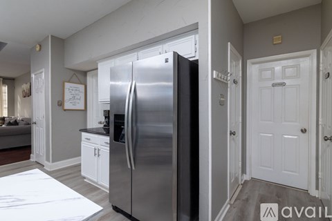 A stainless steel refrigerator in a kitchen with white cabinets and a white door.