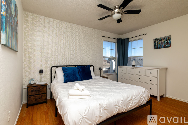 A bedroom with a white bed, a ceiling fan, and a dresser with a mirror.