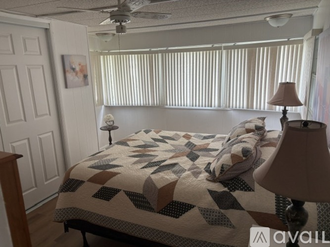 A bedroom with a bed covered in a quilt and a lamp on the side table.