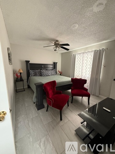 A bedroom with a bed, two chairs, and a ceiling fan.