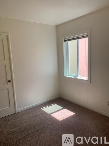 A room with a carpeted floor, a door, and a window with a view of a building outside.