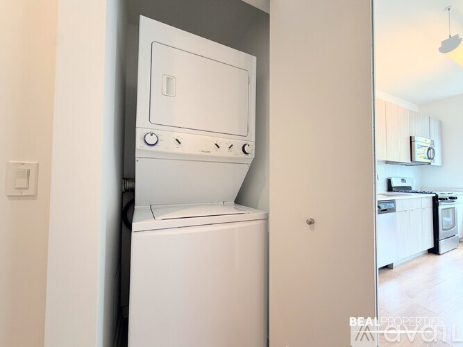 A white dishwasher is in a narrow space between a wall and a kitchen.