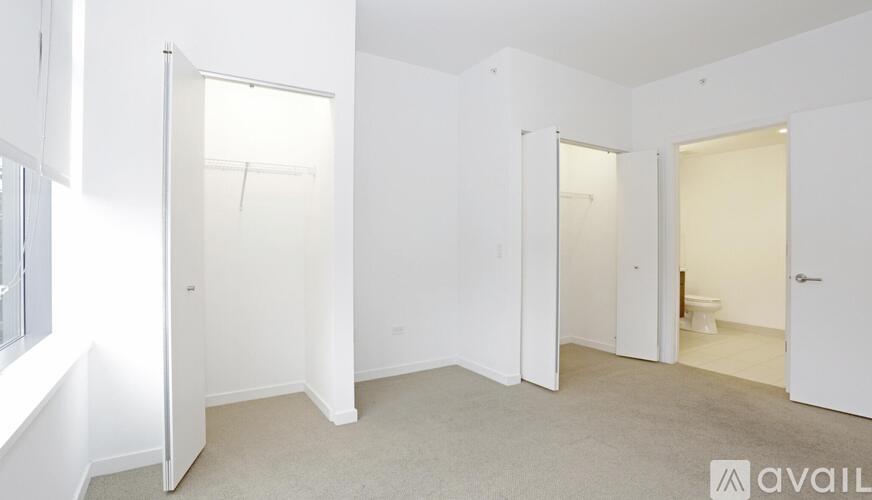 A room with white walls and carpeted floor with a toilet visible in one of the open doors.
