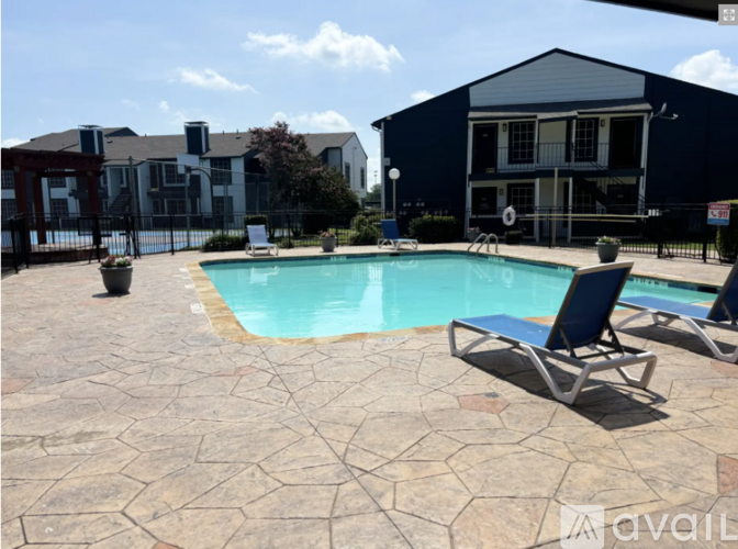 A pool surrounded by a patio with chairs and a building in the background.