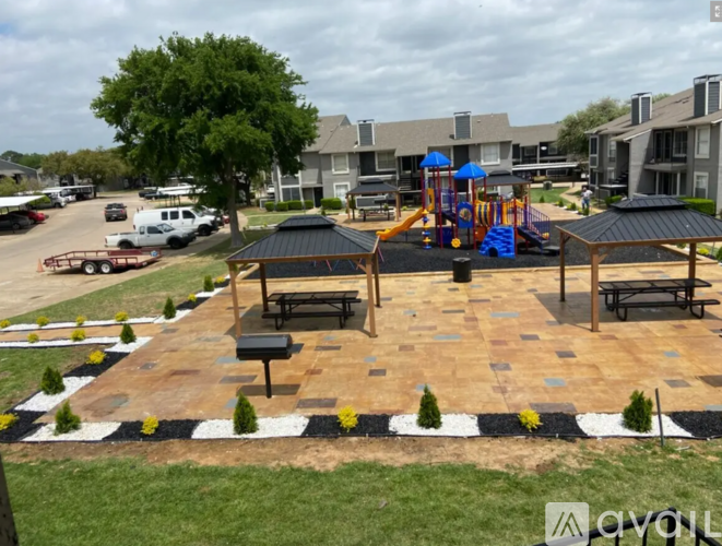 A playground with a slide and a picnic table is surrounded by a brick patio and a grassy area.