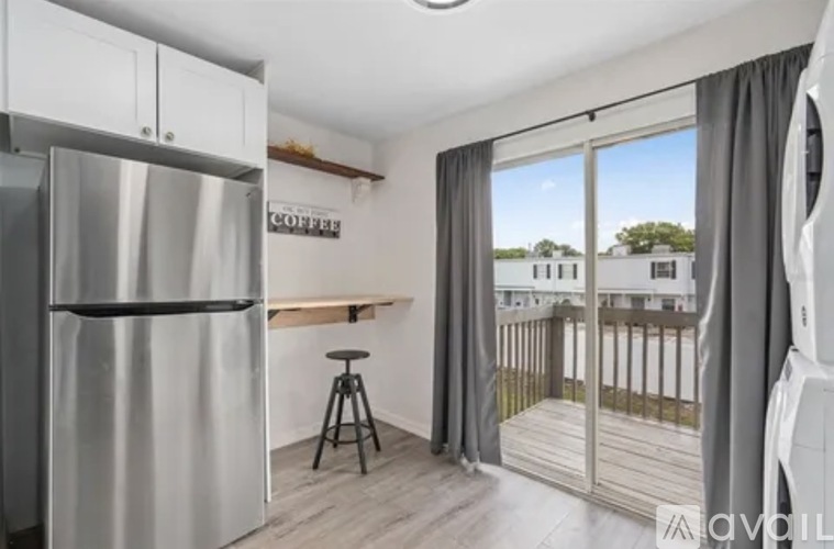 A modern kitchen with a refrigerator, bar stool, and sliding glass doors leading to a balcony.
