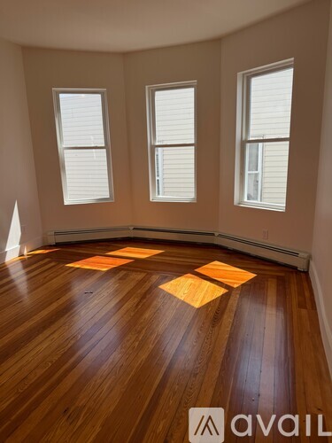 A room with wooden flooring and three windows.