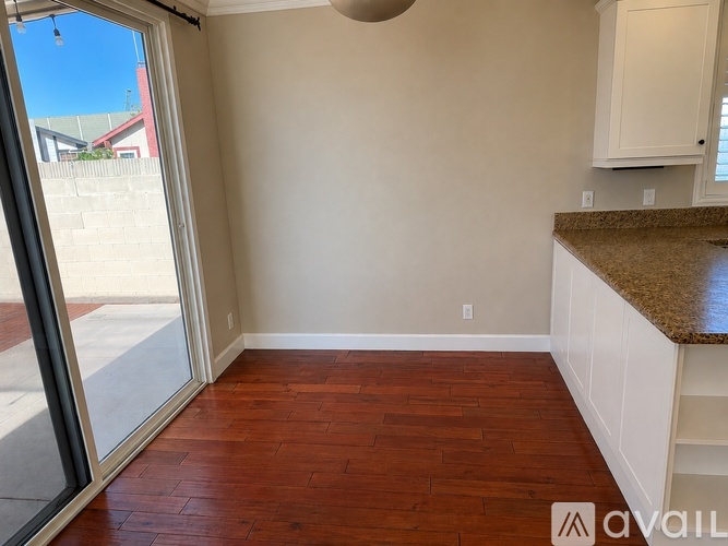 A room with a wooden floor and a kitchen area with white cabinets.