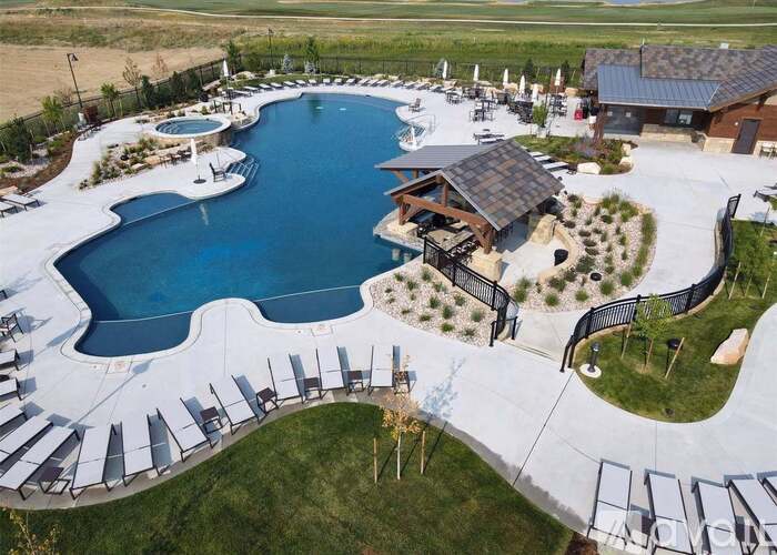 A large outdoor swimming pool surrounded by a fence and lounge chairs.
