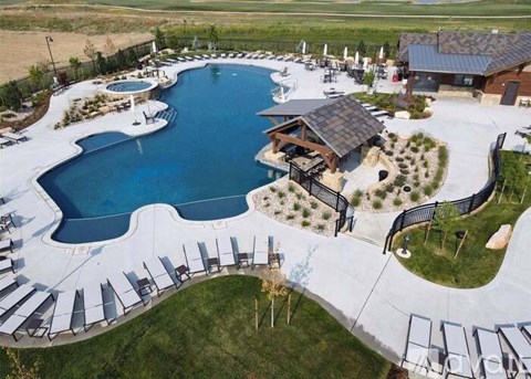 A large outdoor swimming pool surrounded by a fence and lounge chairs.