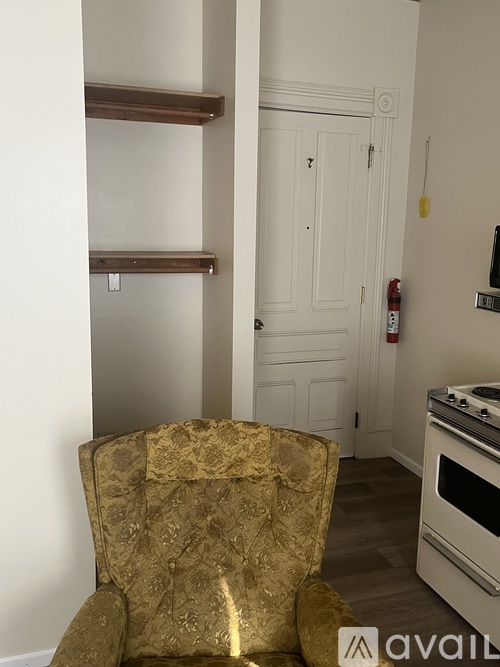 A gold patterned chair is in the foreground of a white wall and a white door.