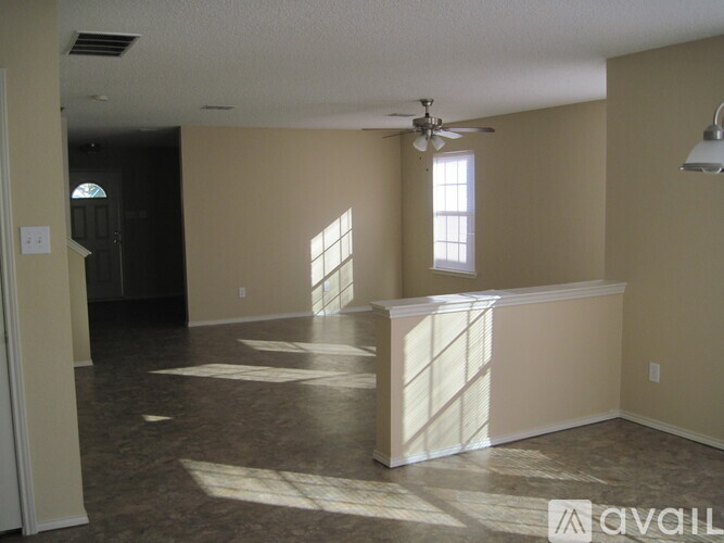 A spacious room with a ceiling fan and sunlight streaming in through the windows.