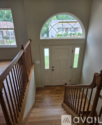 A wooden staircase with a white door and a window with a view of a house.