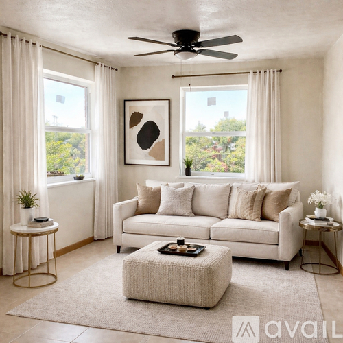 A living room with a white couch, a round ottoman, and a ceiling fan.