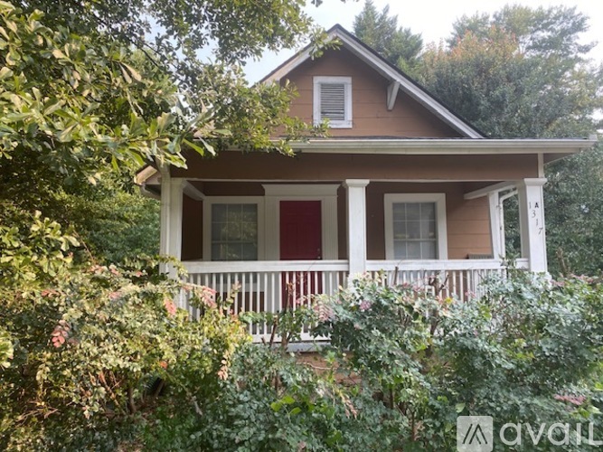 A house with a red door and white columns is surrounded by greenery.
