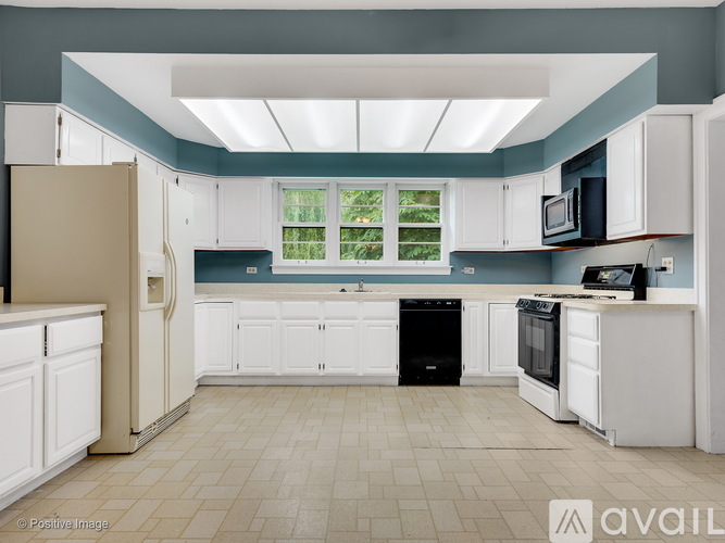A kitchen with white cabinets and appliances, a black dishwasher, and a window with greenery outside.