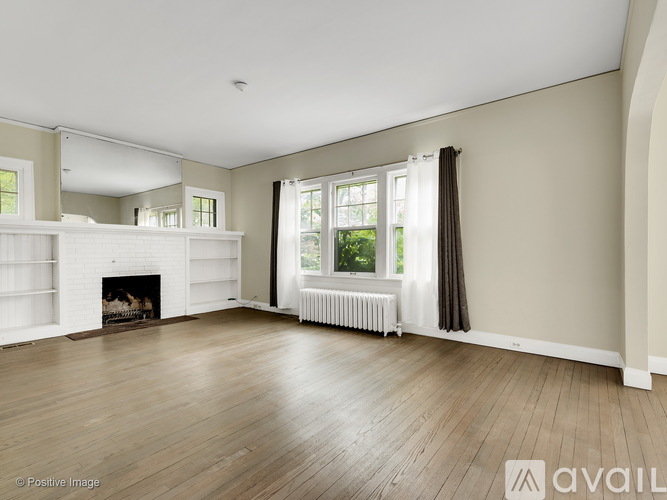 A spacious room with a fireplace and a window with curtains.
